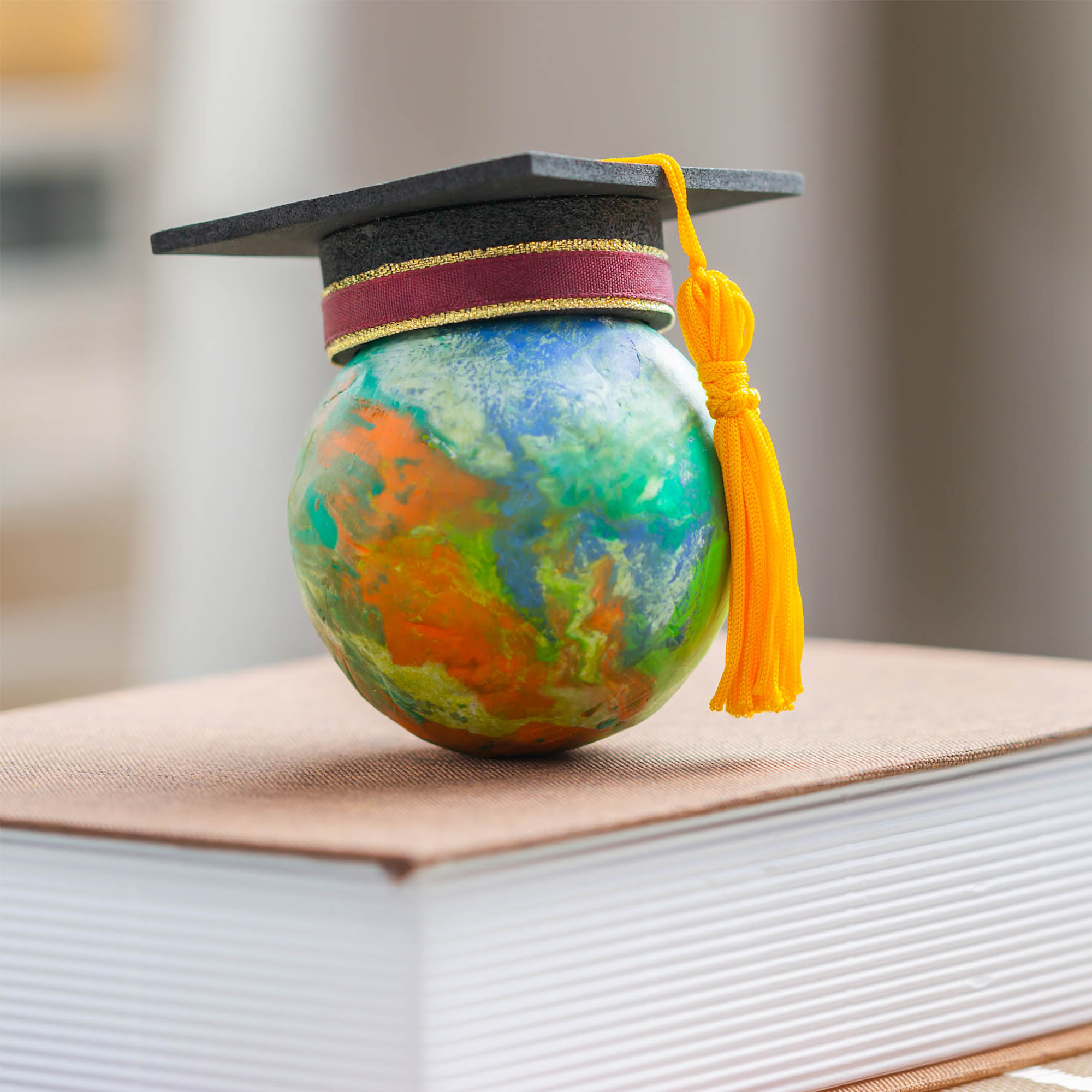 Globe with university graduate cap on top of book