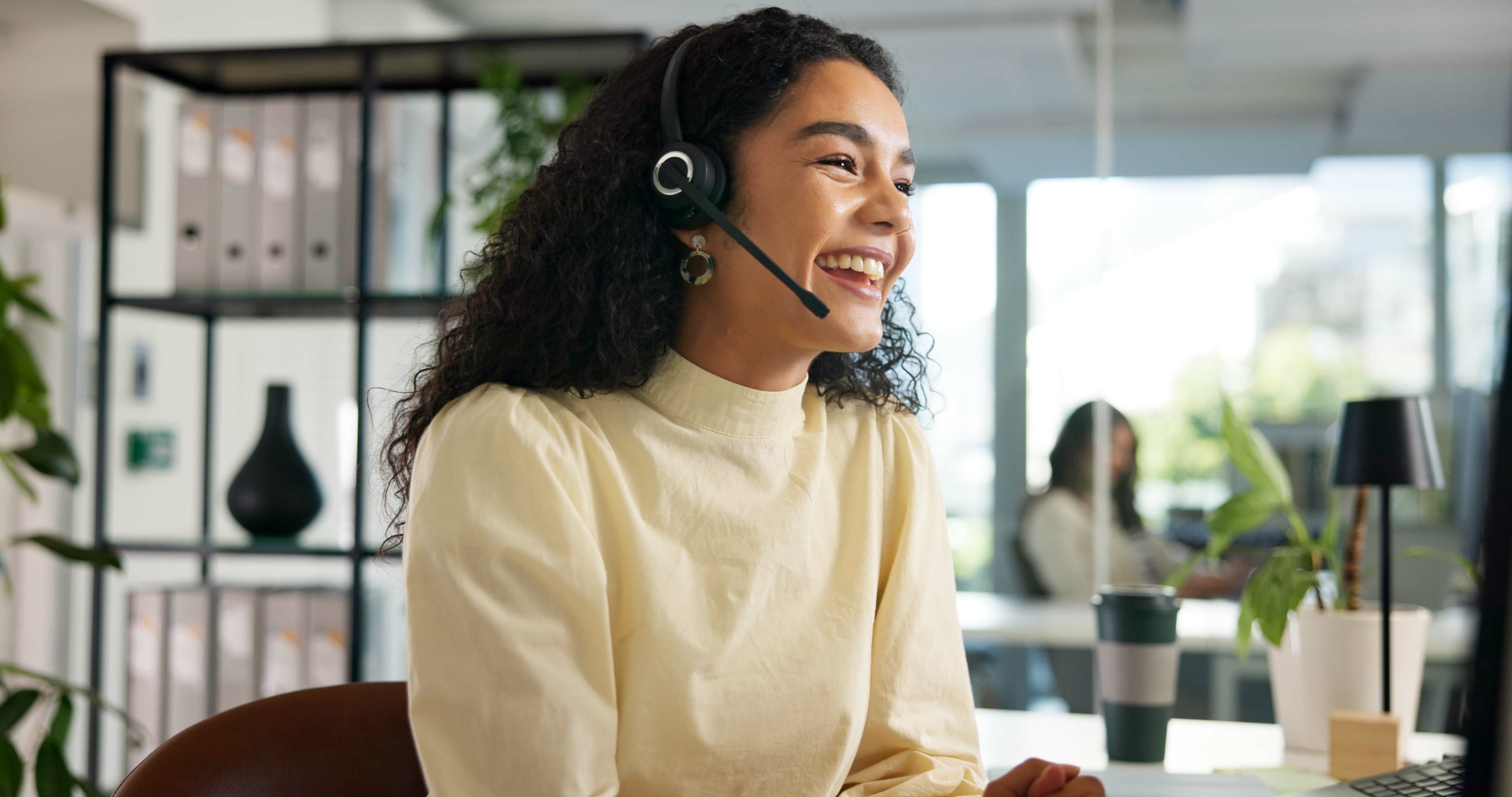 Woman with headphones smiling on phone to customer