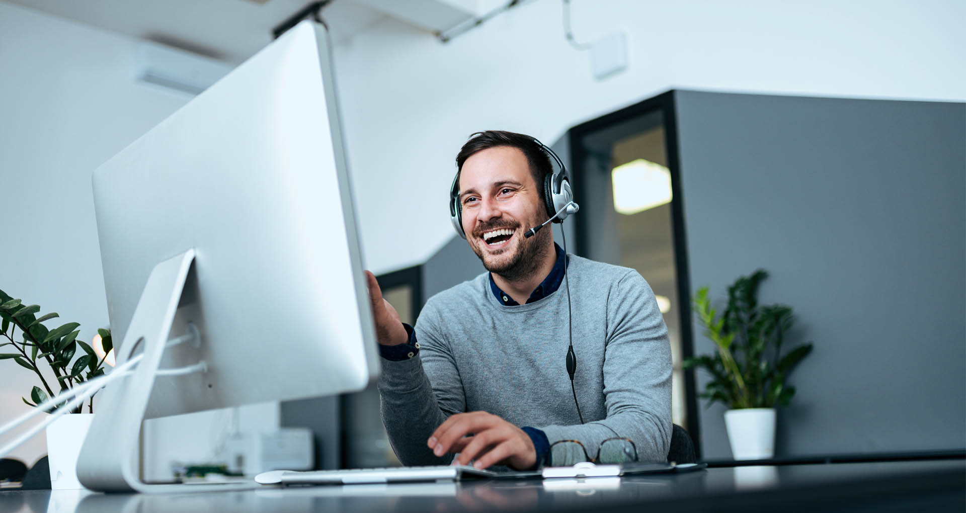 man with Headset smiling at computer screen