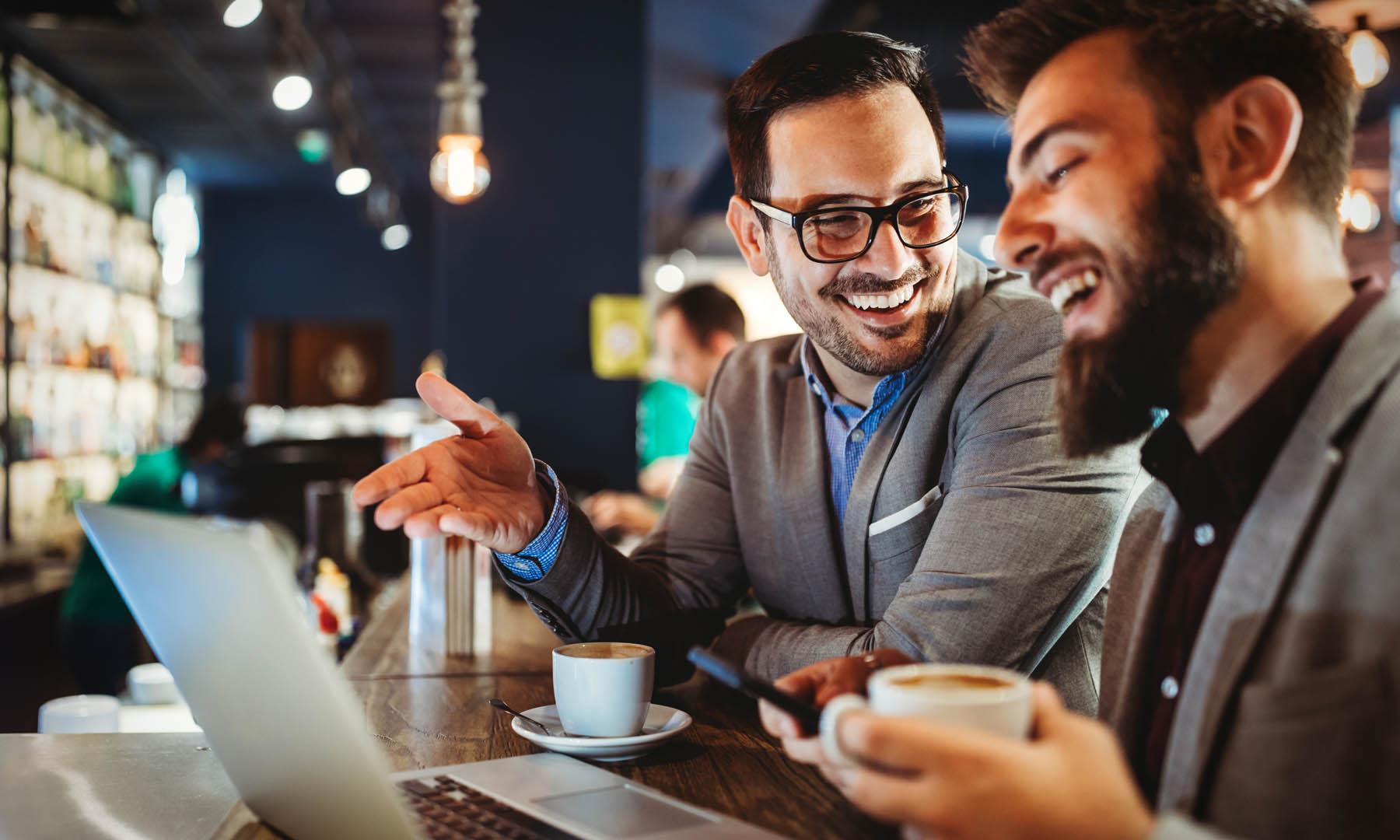 two men in a bar with laptop laughing