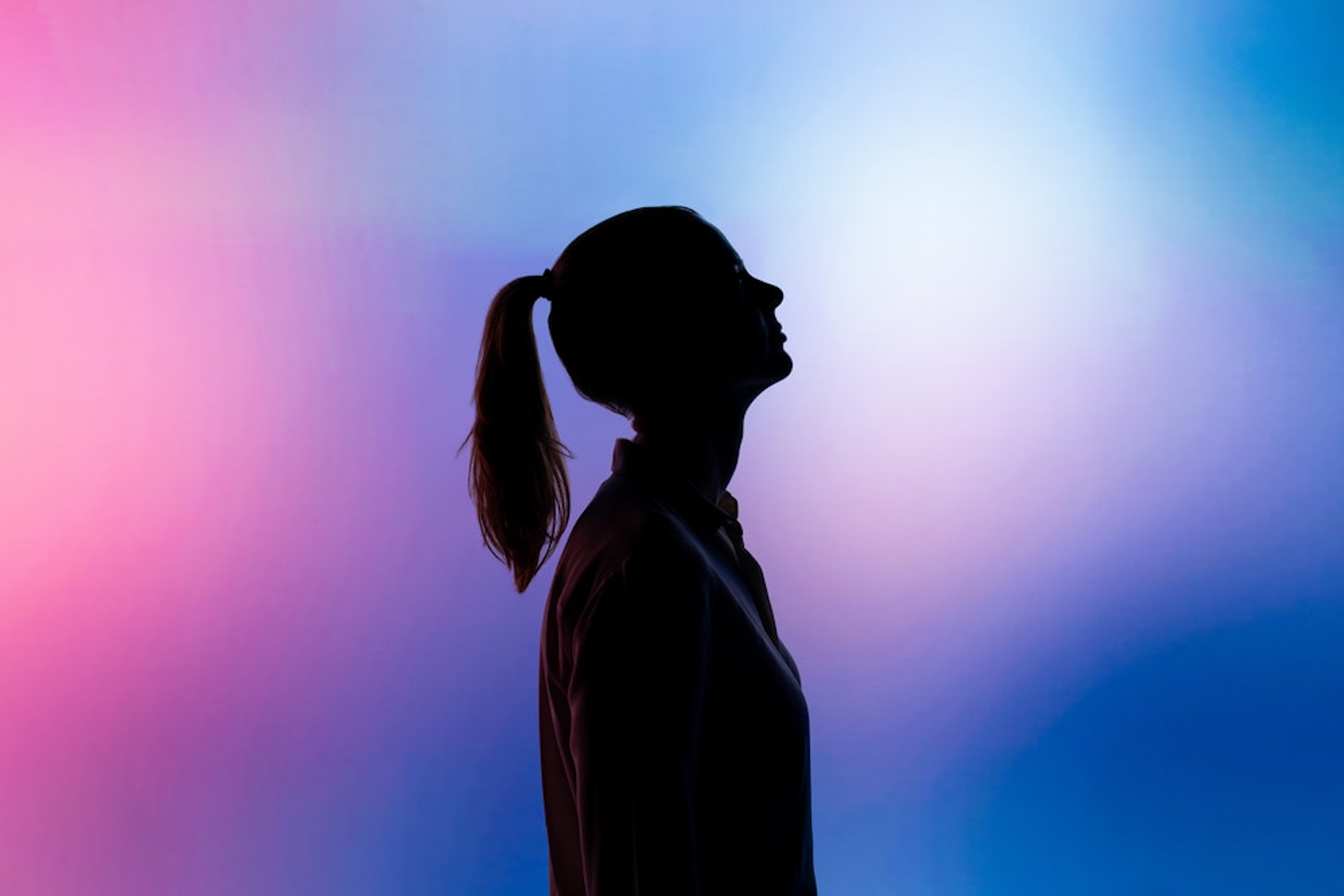 Dark outline of a woman with a ponytail against a colourful hazy background